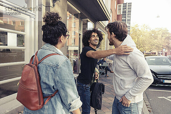 Glückliche männliche Freunde grüßen sich gegenseitig  während sie neben einer jungen Frau vor einem Café stehen