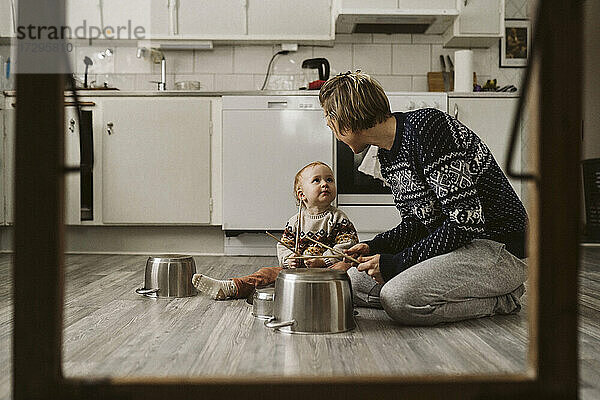 Mädchen schaut Mutter an  während sie mit Essstäbchen in der Küche zu Hause spielt