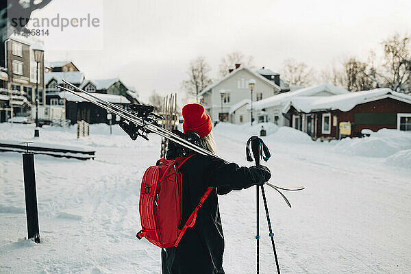 Rückansicht einer jungen Frau  die Skier trägt  während sie im Winter auf Schnee steht