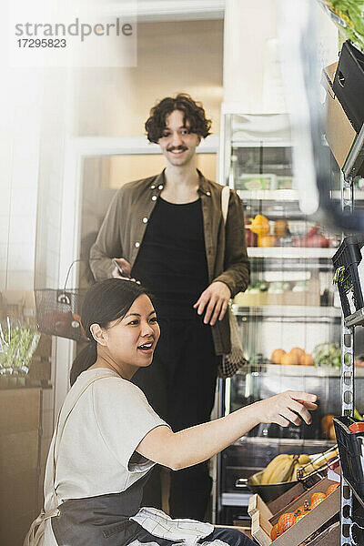 Lächelnder weiblicher Mitarbeiter  der auf ein Regal im Geschäft zeigt