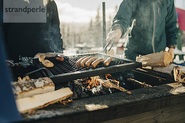 Mittelteil von Freunden bei der Zubereitung von Würstchen auf dem Grill