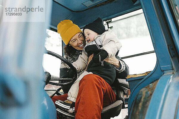 Fröhliche Mutter mit Tochter im Traktor sitzend im Winter