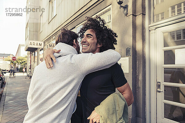 Fröhlich männliche Freunde umarmen einander außerhalb Cafe