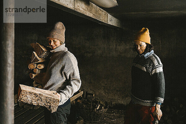 Reife Frau schaut Freundin beim Sammeln von Brennholz im Schuppen stehend an