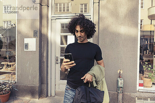 Mid erwachsenen Mann mit lockigem Haar mit Smartphone  während außerhalb Café stehen