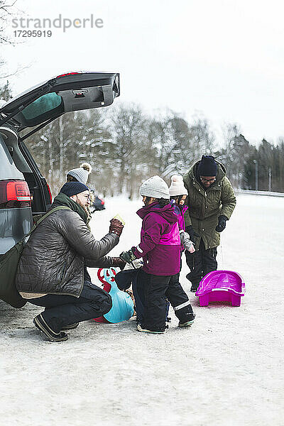 Vater im Gespräch mit Tochter durch Familie Entladen Auto Kofferraum im Winter