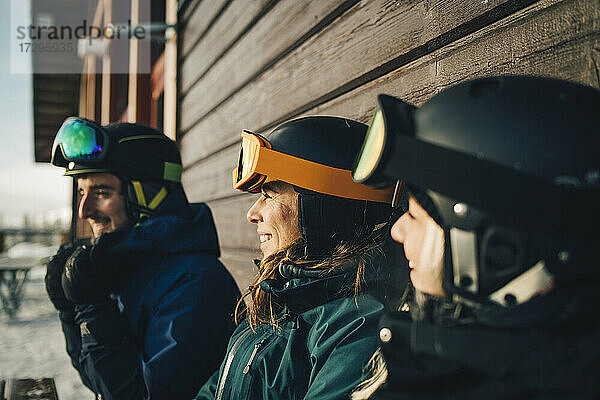 Lächelnde Freunde mit Sporthelmen im Skigebiet bei Sonnenuntergang