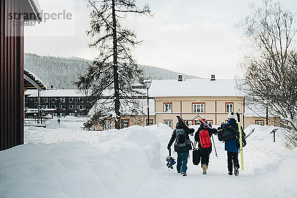 Volle Länge Rückansicht von Freunden tragen Rucksack beim Gehen auf Schnee im Skigebiet