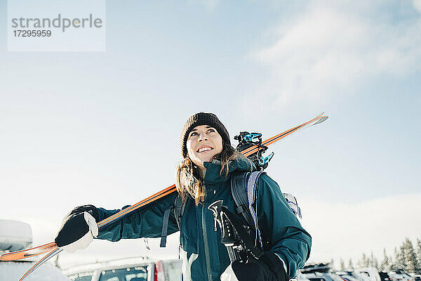 Lächelnde Frau trägt Skier im Winter gegen den Himmel