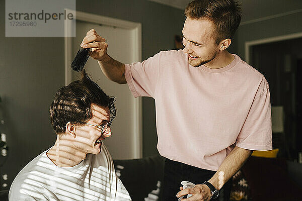 Junger Mann kämmt die Haare eines männlichen Freundes  während er zu Hause sitzt