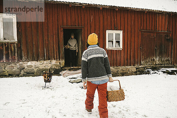 Ältere Frau trägt Korb beim Gehen in Richtung Hütte im Winter
