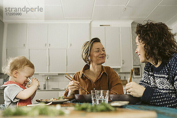 Lächelndes lesbisches Paar mit Tochter beim Mittagessen zu Hause