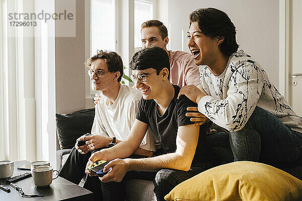 Lächelnde multiethnische männliche Freunde spielen Videospiel im Wohnzimmer