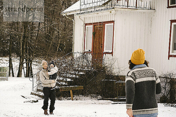 Ältere Frau zu Fuß in Richtung lächelnde Freundin trägt Tochter auf Schnee