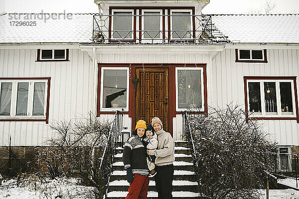 Porträt von glücklichen lesbischen Paar mit Tochter gegen Haus im Winter