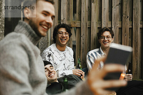Lächelnde männliche Freunde nehmen Selfie durch Smartphone in Balkon