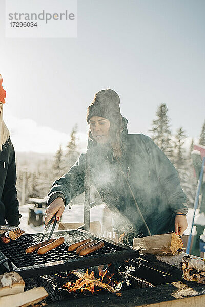 Freundinnen bereiten im Winter Würstchen auf dem Grill zu