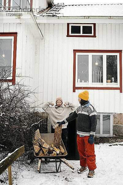Reife Frau Blick auf Freundin flexing Muskeln stehen von Schubkarre auf Schnee gegen Haus