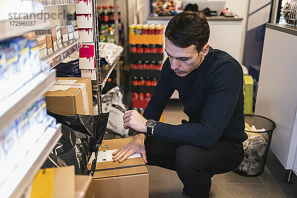 Männlicher Unternehmer  der eine Box analysiert  während er im Laden arbeitet