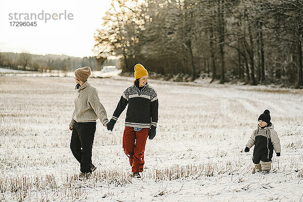 Homosexuelles Paar hält die Hände beim Spaziergang mit Tochter auf Schnee im Winter