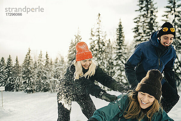 Glückliche männliche und weibliche Freunde spielen im Skigebiet im Winter