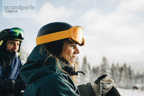 Lächelnde Frau trägt eine Skibrille und hält eine Kaffeetasse im Winter