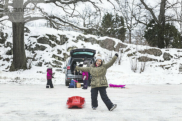 In voller Länge von glücklichen Mädchen stehen mit Schlitten auf Schnee gegen Familie