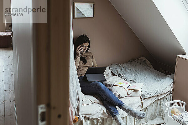 Geschäftsfrau spricht auf Smartphone  während mit digitalen Tablet im Schlafzimmer