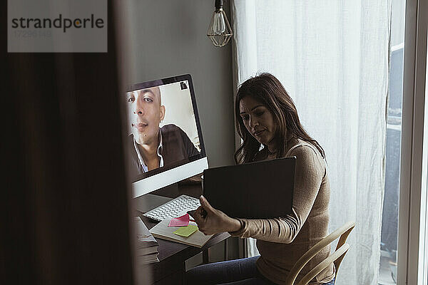 Geschäftsfrau zeigt Laptop an männlichen Profi auf Videoanruf im Home-Office