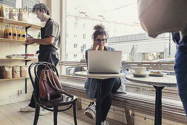 Weiblicher Kunde benutzt Laptop von männlichem Besitzer  der im Café arbeitet