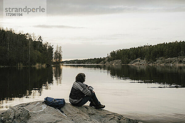 Weiblicher Wanderer bewundert See  während er auf einem Felsen gegen den Himmel sitzt