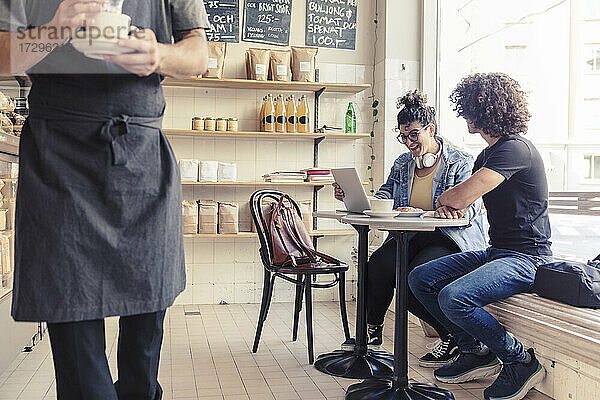 Glückliche weibliche und weibliche Freunde diskutieren über Laptop im Cafe