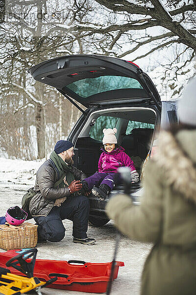 In voller Länge von Vater hilft Tochter mit Schuh sitzen im Kofferraum des Autos im Winter