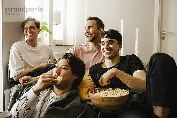 Lächelnde männliche Freunde  die Popcorn essen  während sie zu Hause Sport schauen