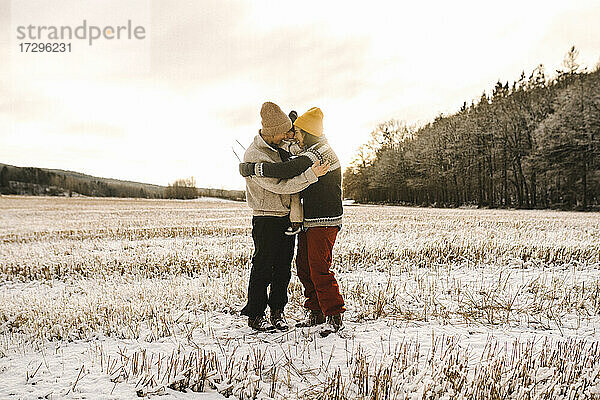 Glückliche Homosexuell Paar umarmt Tochter stehen auf Schnee während des Sonnenuntergangs