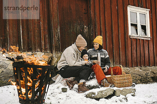 Reife Frau sitzt mit Freundin Fütterung Tochter gegen Hütte im Winter