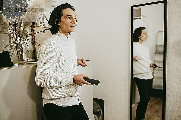 Mid erwachsenen Mann mit Smartphone stehen durch Spiegel zu Hause