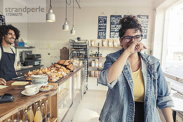 Männlicher Besitzer schaut auf fröhliche weibliche Kundin im Café