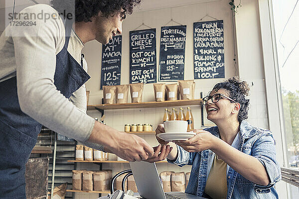 Männlicher Kellner serviert Kaffee zu fröhlichen weiblichen Kunden im Café
