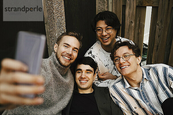 Lächelnde multiethnische männliche Freunde  die ein Selfie mit dem Handy auf dem Balkon machen