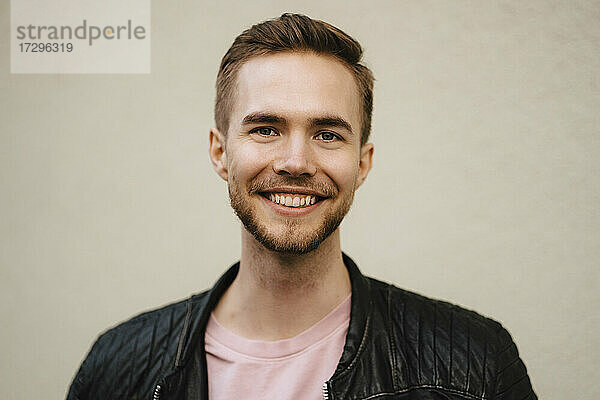 Lächelnder junger Mann mit Bartstoppeln an der Wand