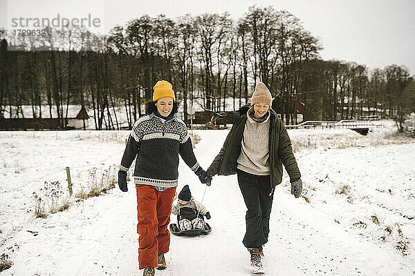 Lächelnde lesbische Paar Ziehen Tochter auf Schlitten im Winter
