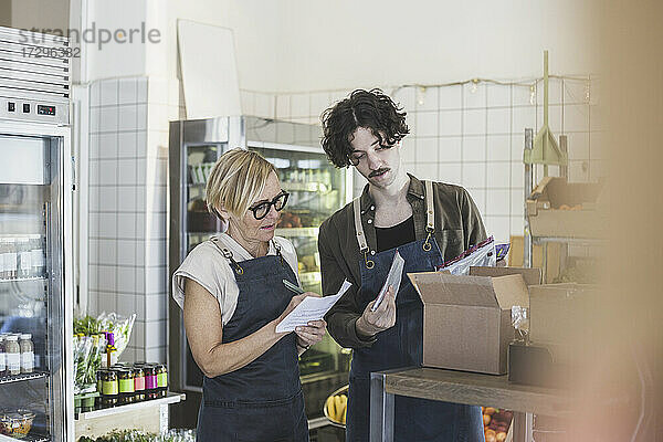 Weibliche Unternehmerin macht sich Notizen  während ein männlicher Mitarbeiter ein Lebensmittelpaket im Laden zeigt