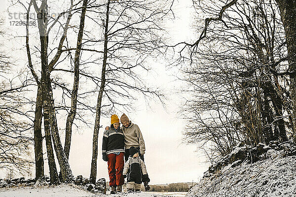 Lächelnde lesbische Mütter mit Tochter zu Fuß inmitten von kahlen Bäumen im Winter