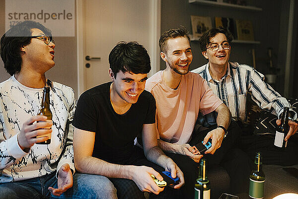 Lächelnde männliche Freunde mit Bierflasche spielen Videospiel zu Hause