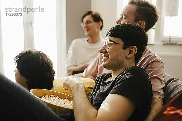 Multi-ethnische männliche Freunde essen Popcorn  während sie im Wohnzimmer Sport schauen