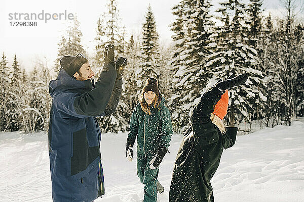 Fröhlich Mann und Frau geben High-Five von weiblichen Freund beim Spielen im Schnee im Skigebiet