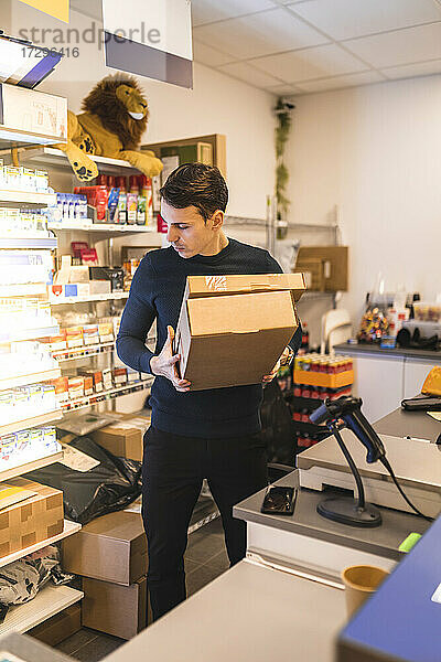Männlicher Ladenbesitzer trägt Kartons  während er an der Kasse im Laden steht