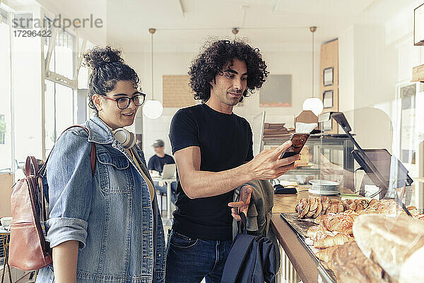 Junge Frau schaut auf männlichen Freund mit Smartphone im Café