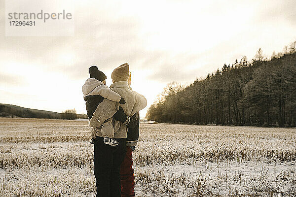 Lesbisches Paar mit Tochter stehend auf Schnee bei Sonnenuntergang